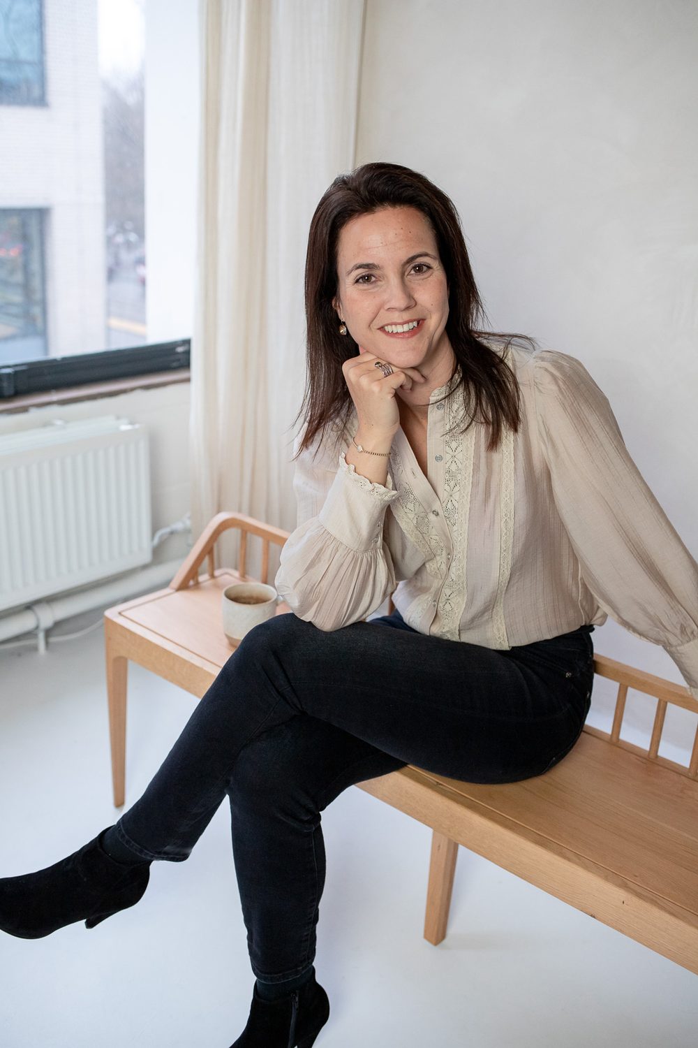 Monique Vekemans zit op een houten bankje, met haar hand bij haar kin