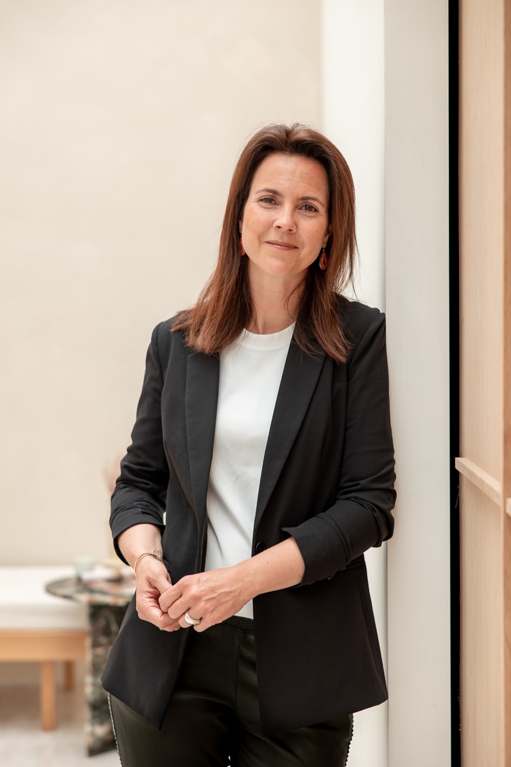 Monique Vekemans leunt rustig tegen een muur in een licht interieur