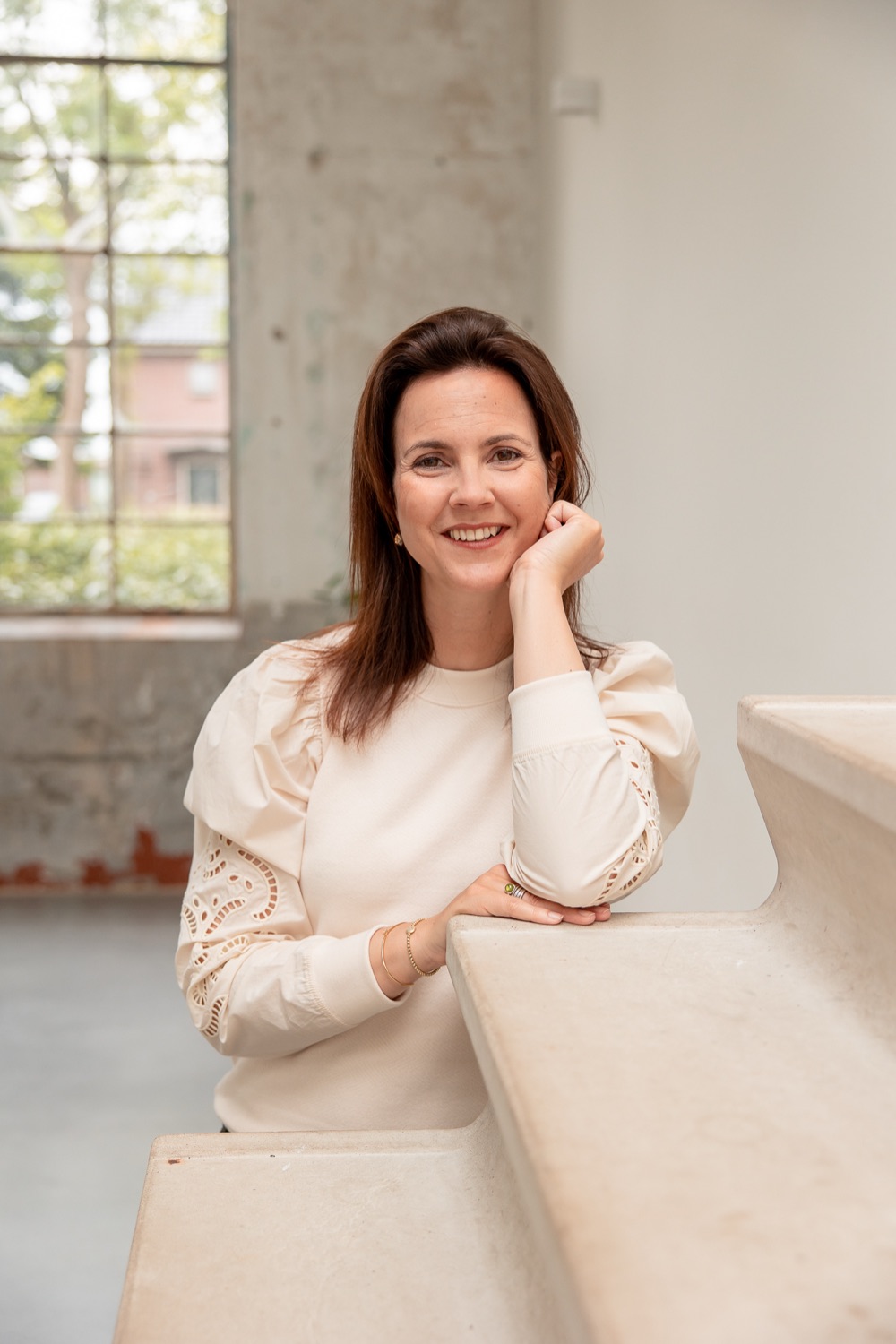 Monique Vekemans leunt lachend op een betonnen trap