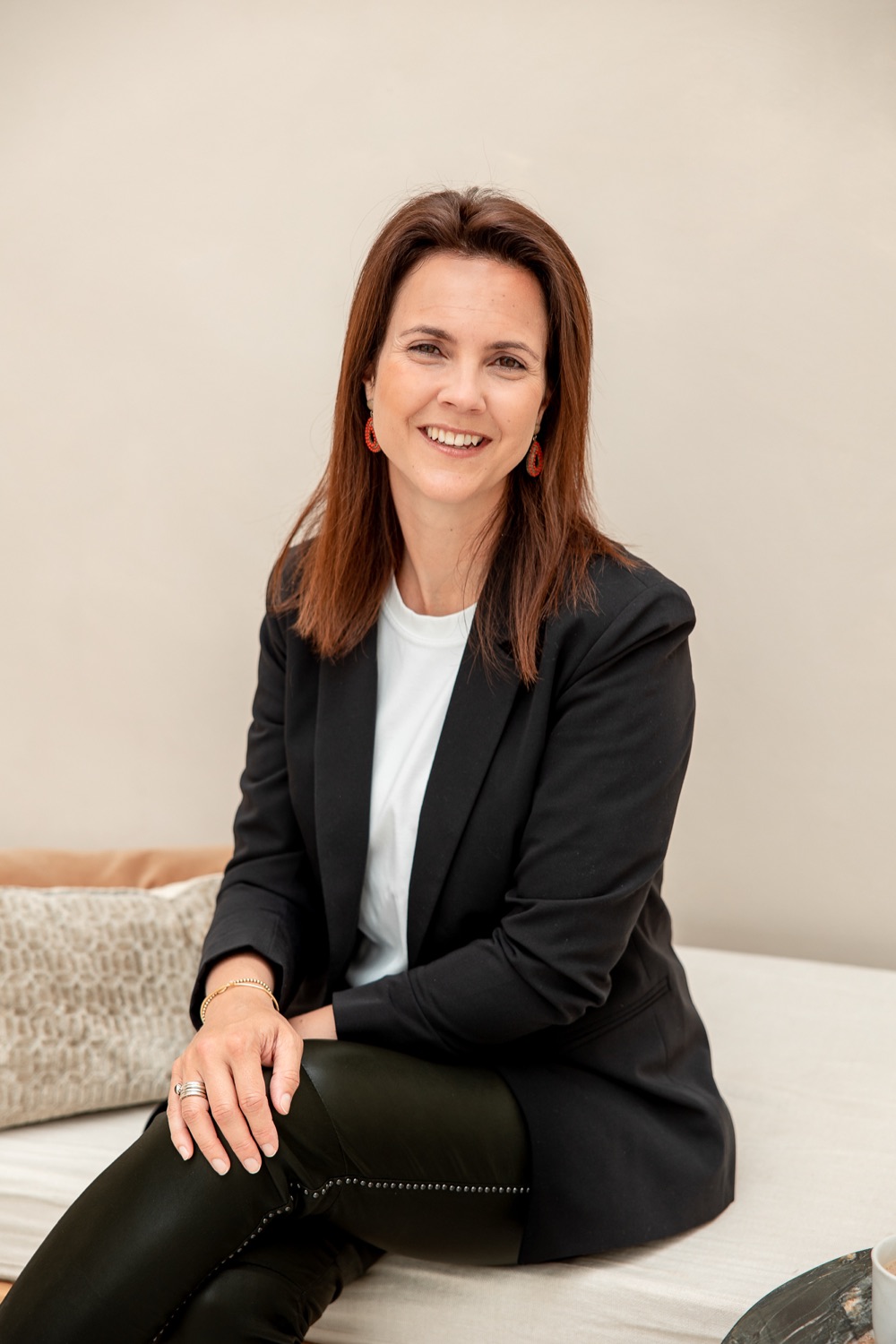 Monique Vekemans zit lachend op een bank in een licht interieur